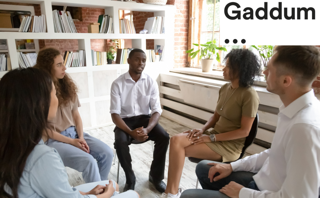 Gaddum logo. A group of 5 people sat on chairs in a circle