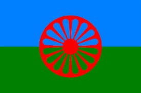 The Gypsy, Roma and Traveller History Month flag with the red emblem of GRT hertiage in red, with blue on the top half of the flag and green on the bottom half